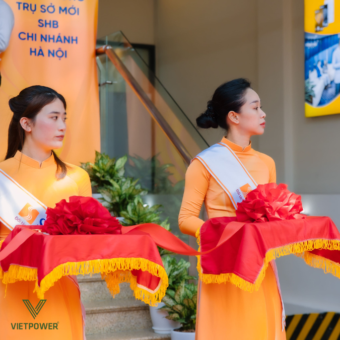 Hai nữ lễ tân mặc áo dài đứng cầm khay cắt băng khánh thành tại trụ sở mới của SHB chi nhánh Hà Nội