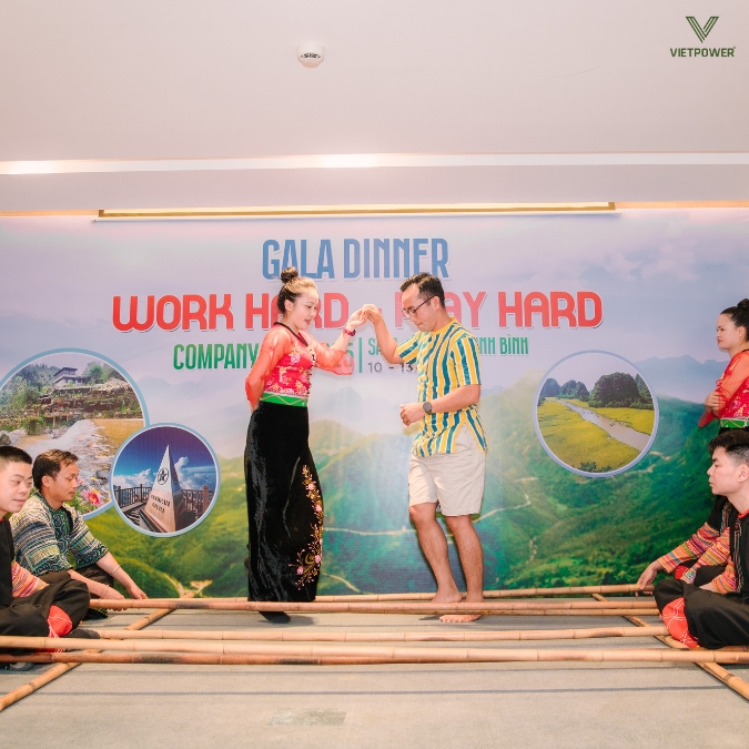 Vũ công nắm tay hướng dẫn đồng nghiệp bước nhịp nhàng qua khung sạp tre