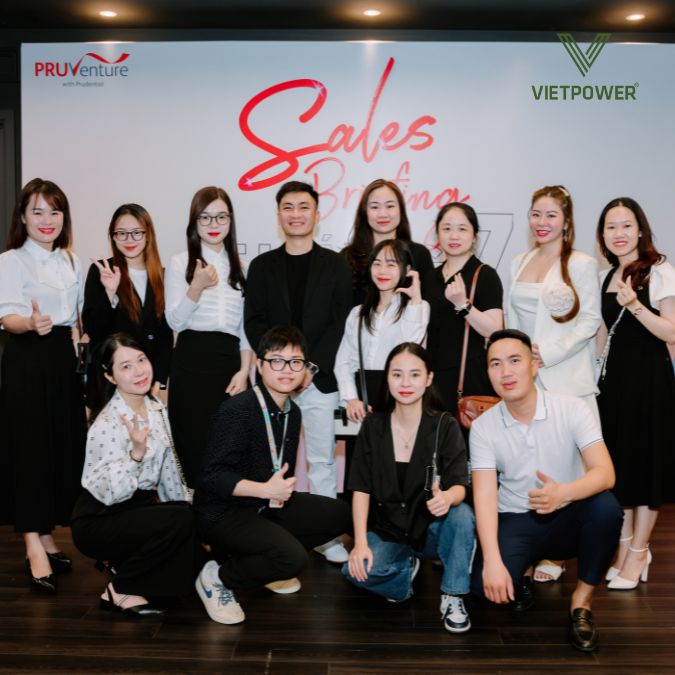Một nhóm người đứng và ngồi cười, chụp ảnh lưu niệm trước backdrop có logo Pruventure và dòng chữ "Sales Briefing"