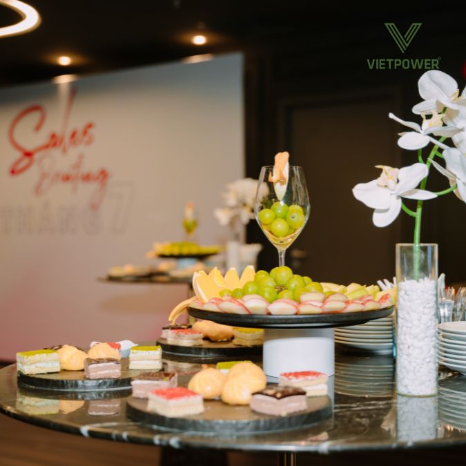 Bàn tiệc ngọt với nhiều loại bánh, trái cây được bày trí hấp dẫn, cùng bình hoa lan trắng tại hội thảo Pruventure